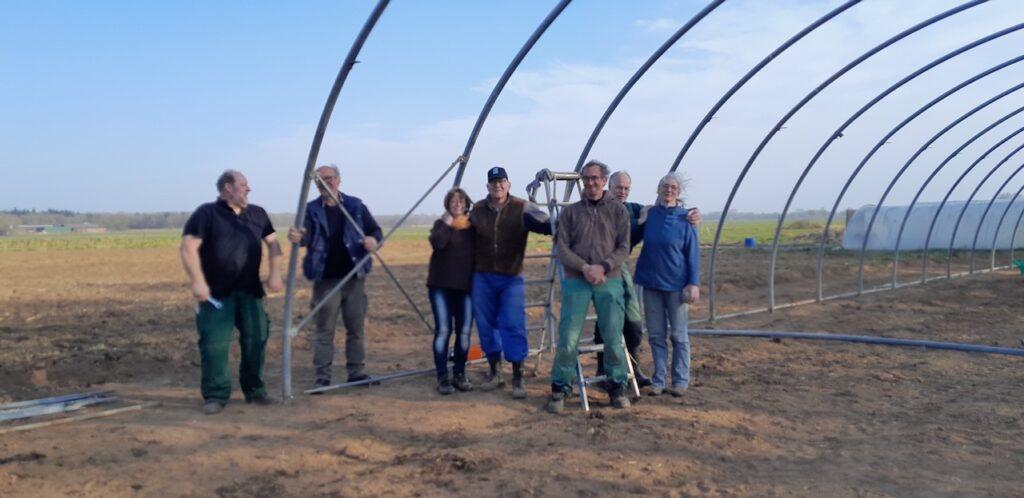 Gruppe Menschen auf Acker unter Folientunnel Gerüst